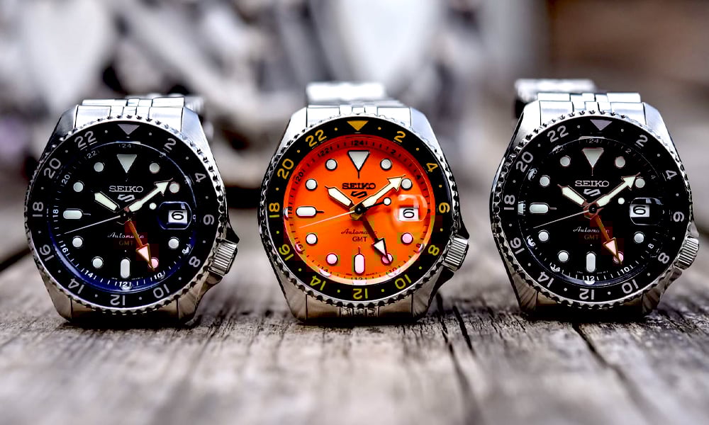 Three Seiko watches with different colored faces on a wooden surface